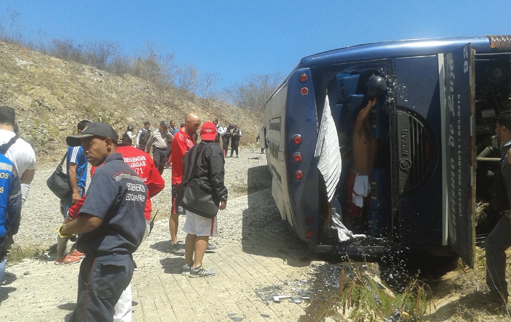 Emergency personnel and members of Agentina's Huracan soccer team, in red shirts and black shorts, mill around the wreck of the bus that was transporting the team to the airport, after it lost its brakes, lost control and flipped over, in Caracas.