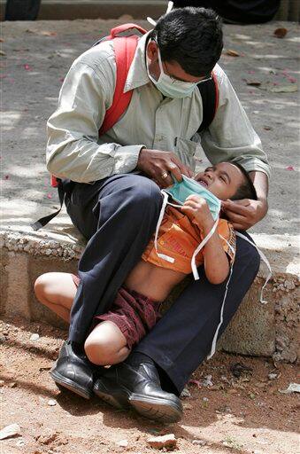 A man forces his child to wear a face mask as they wait to get themselves examined at a swine flu examination center at a government hospital in Bangalore, India, Monday, Aug. 10, 2009. According to media reports, two more people infected with swine flu have died, raising the country`s death toll from the virus to six.