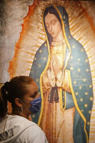 A woman wearing a surgical facemask stands next to an image of the Virgin of Guadalupe, Mexico`s patron saint, at the Basilica of Guadalupe in Mexico City, Sunday, April 26, 2009.