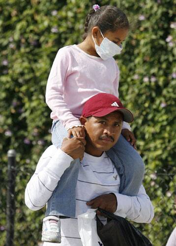 A man carries a young girl wearing a mask as they enter the U.S. from Mexico at the San Ysidro Port of Entry in San Diego Sunday, April, 26, 2009.