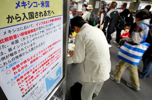 Arriving passengers walk past an instruction board describing symptoms of swine flu at an arrival gate at Narita International Airport in Narita, east of Tokyo, Japan, Sunday, April 26, 2009.