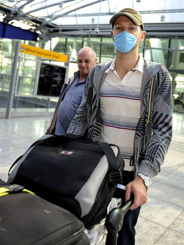 Teacher Alistair Dixon, returning home from Mexico, wears a face mask as he pushes his luggage beside his father Stanley, background, after landing at London`s Heathrow airport Sunday April 26, 2009.