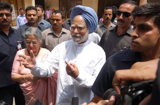 Indian Prime Minister Manmohan Singh, center, accompanied by wife Gursharan Kaur, left, gestures to media after casting his vote in Gauhati