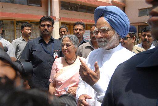 Indian Prime Minister Manmohan Singh, accompanied by wife Gursharan Kaur, center, gestures to media after casting his vote in Gauhati, India