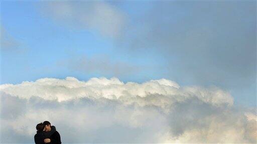 A couple hug in front of white clouds during sunny weather on the visitor platform near at Germany highest mountain Zugspitze (2.962 meter) near Garmisch-Partenkirchen, southern Germany