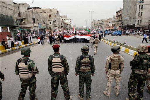 Iraqi Army soldiers stand guard as supporters of anti-U.S. Shiite cleric Muqtada al-Sadr march in central Baghdad, Iraq, marking the sixth anniversary of the fall of the Iraqi capital to American troops.