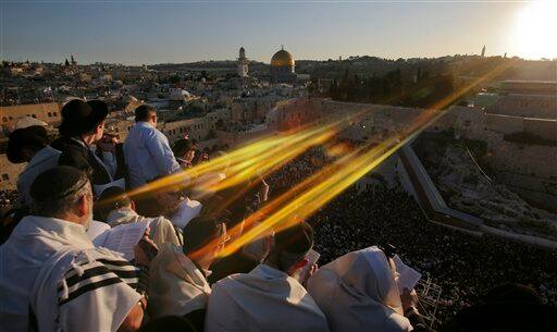 The sun flares across the scene as Ultra Orthodox Jewish men wrapped in prayer shawls participate in the special 