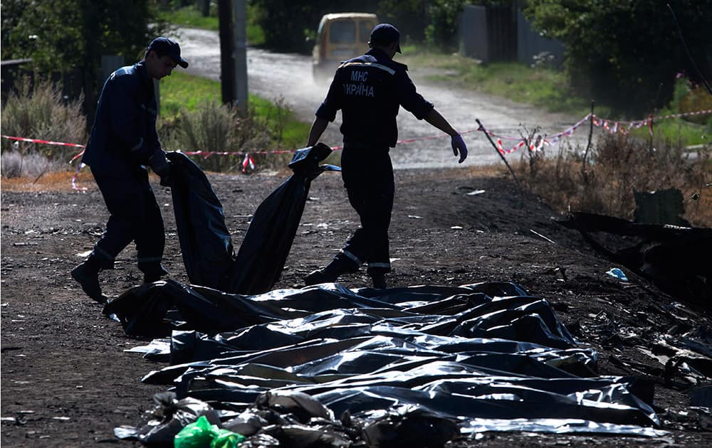 Ukrainian Emergency workers carry a victim`s body in a plastic bag as other bodies are laid on the ground nearby at the crash site of Malaysia Airlines Flight 17 near the village of Hrabove, eastern Ukraine, Donetsk region, eastern Ukraine.