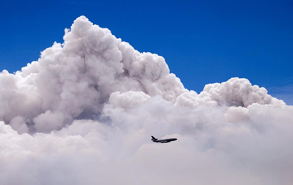 A DC-10 air tanker is dwarfed by the tip of a rising smoke cloud as the plane prepares to drop fire retardant over a wildfire near Carlton, Wash. 