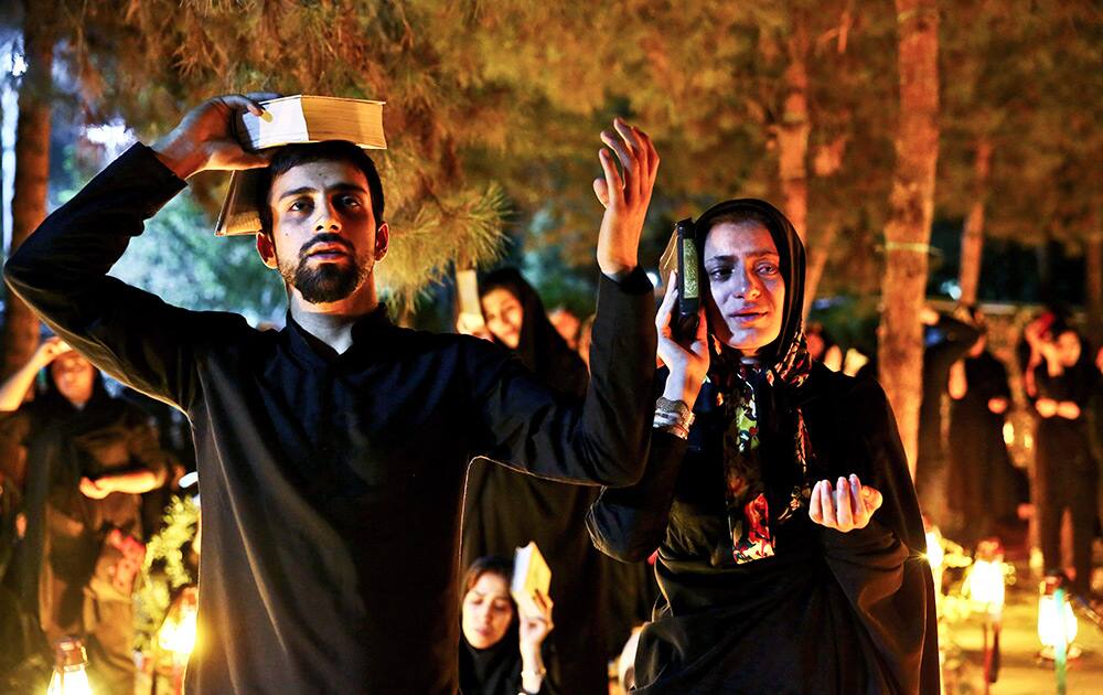 Iranian Shiite Muslims pray as they place the Quran, Islam`s holy book, on their heads during a religious ceremony at the graves of soldiers who were killed during 1980-88 Iran-Iraq war, at the Behesht-e-Zahra cemetery, during the holy fasting month of Ramadan, just outside Tehran, Iran.