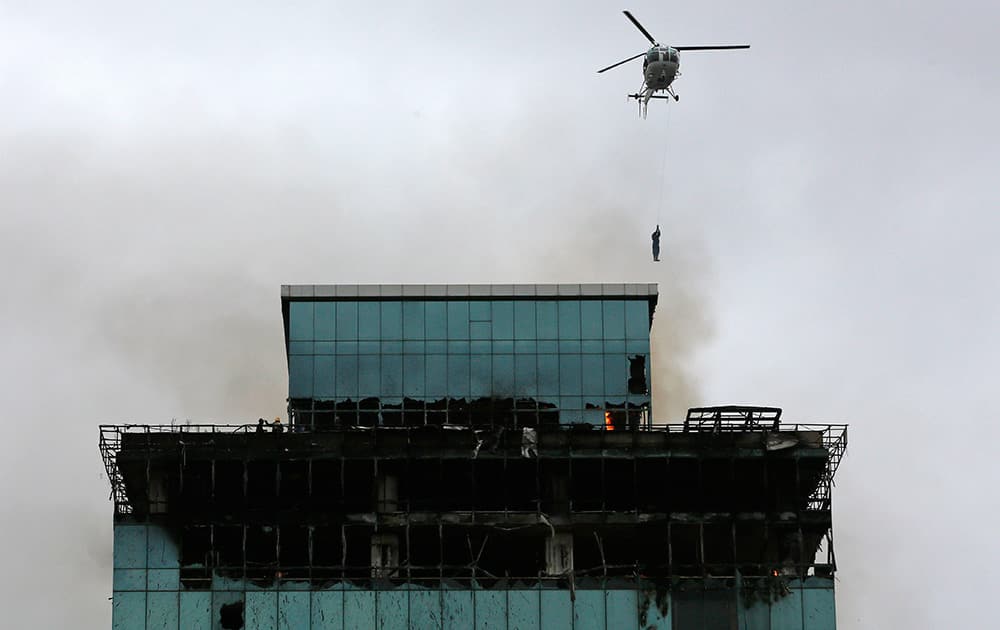 A Navy sailor descends from a helicopter to rescue a fireman trapped in a building on fire in Mumbai. One fireman was killed and several others injured in a fire that broke out in a commercial building Friday, according to a news agency.