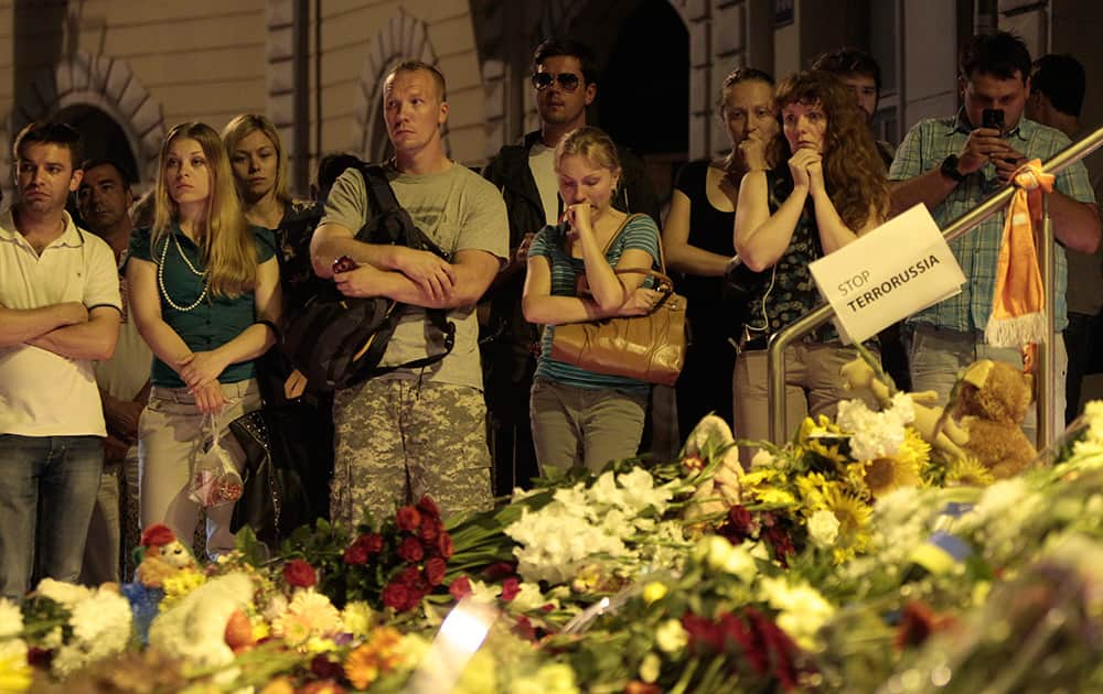 People stand near flower tributes placed outside the Dutch embassy to commemorate victims of Malaysia Airlines plane crash in Kiev, Ukraine.