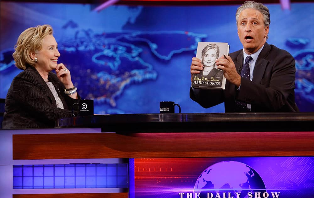 Former US Secretary of State Hillary Rodham Clinton watches as host Jon Stewart holds a book by Clinton during a taping of `The Daily Show with Jon Stewart,`  in New York. 