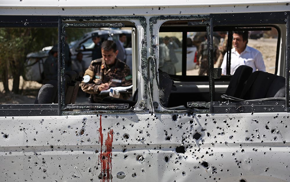 Afghan security personnel investigate a damaged minivan which was hit by a remote controlled bomb on the outskirts of Kabul, Afghanistan.