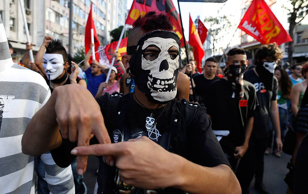 A masked demonstrator signals an anarchy sign during an Anti-World Cup protest near Maracana stadium where the final World Cup game is taking place in Rio de Janeiro, Brazil.