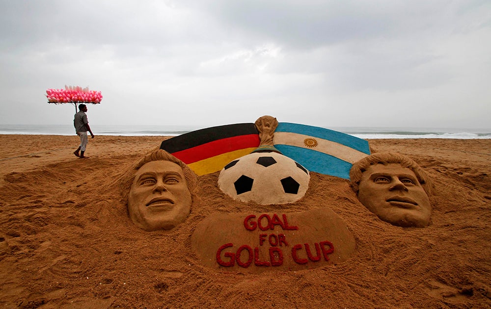 A candy floss vendor walks past a sand sculpture depicting the Argentinian and German flags and soccer players created on the eve of the soccer World Cup final, in Puri, India.