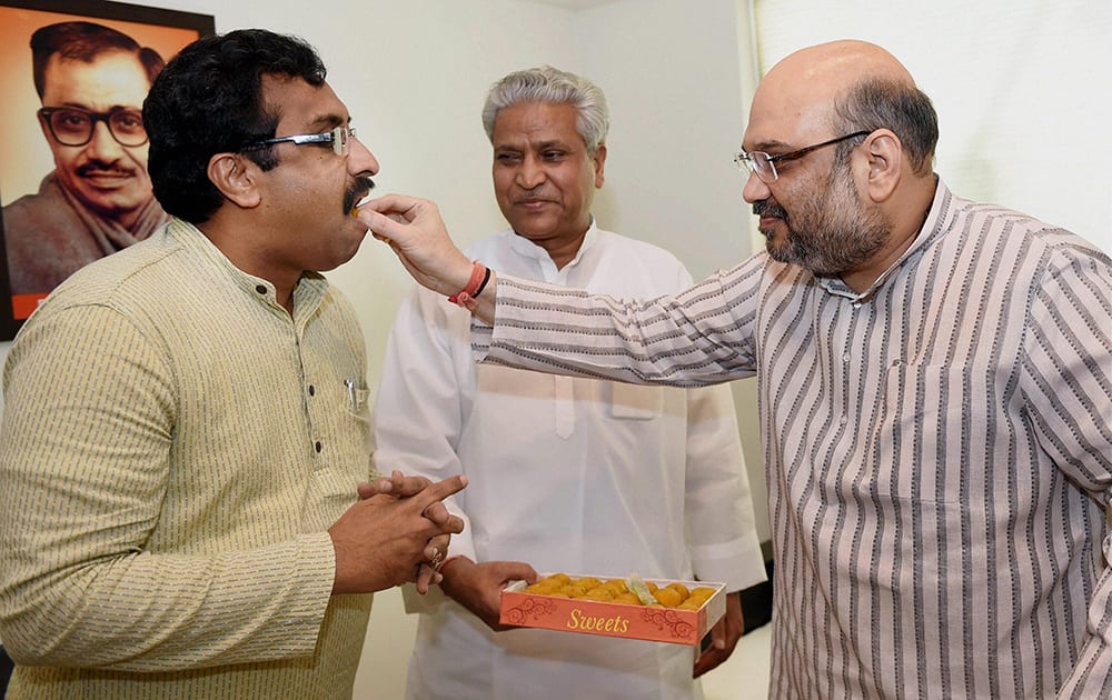 New BJP President Amit Shah offers sweets to the RSS spokesman Ram Madha after he joined the party at party headquarters in New Delhi.