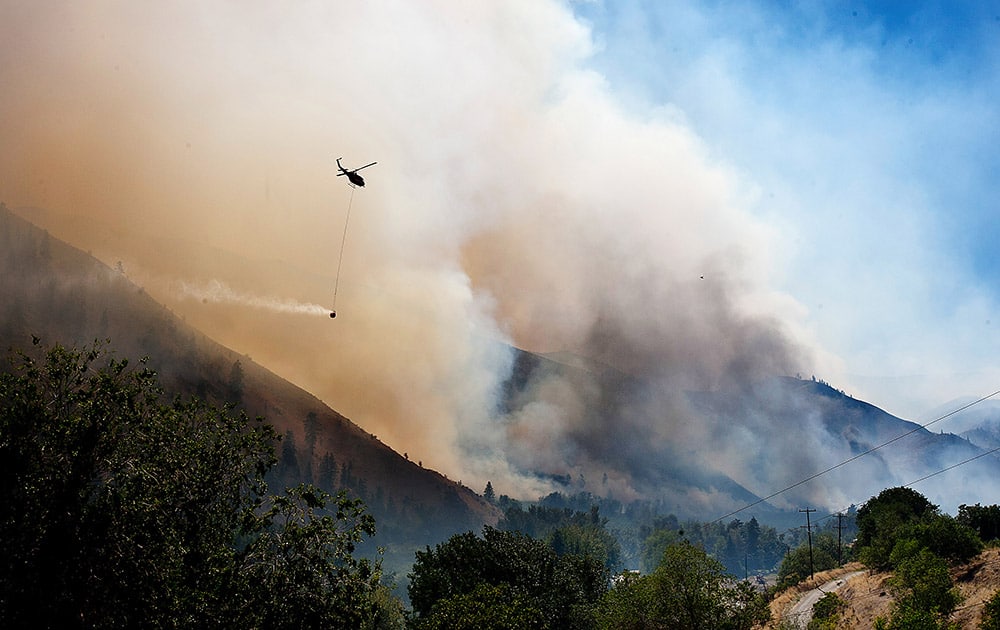 As smoke and fire blow through the lower Entiat Valley near Entiat, Wash., on Wednesday afternoon, a helicopter with a bucket of water flies to the fire to drop its load. 