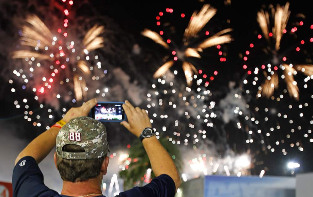 A NASCAR fan takes photos during a fireworks display after the Sprint Cup series auto race was postponed at Daytona International Speedway in Daytona Beach.