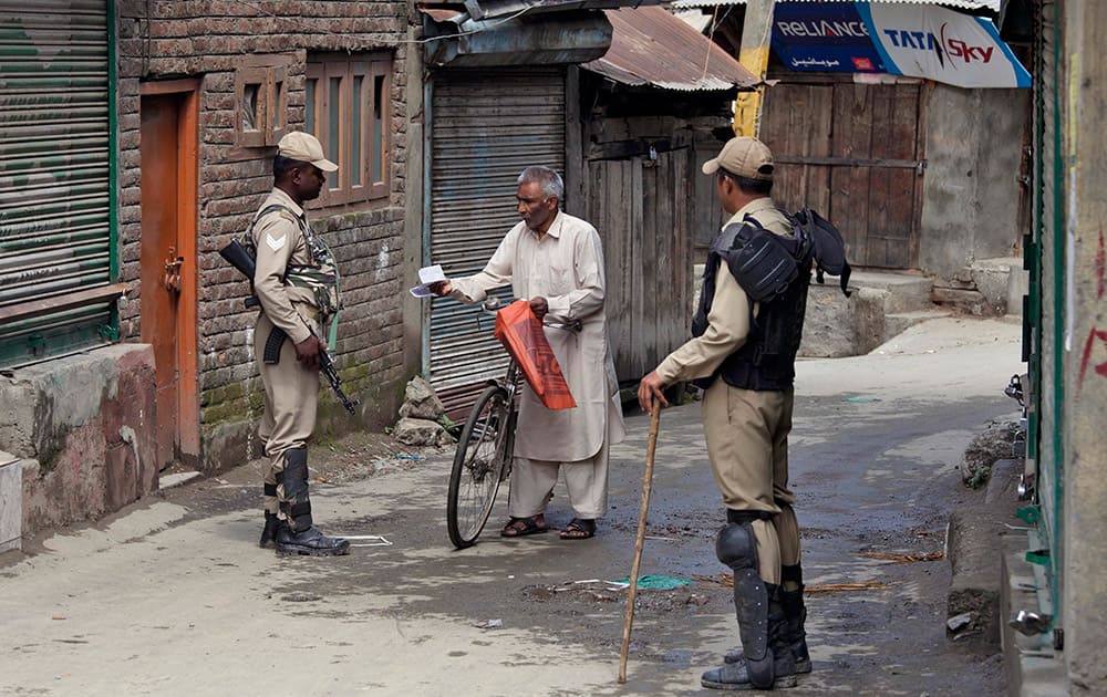 An Indian paramilitary soldier checks medical prescription papers of a man as they question him during restrictions in Srinagar.