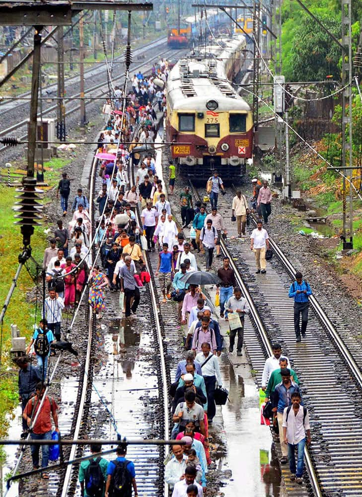 Commuters walk after local train stoped due to flooding at railway tracks during rain at Central Railway in Mumbai.