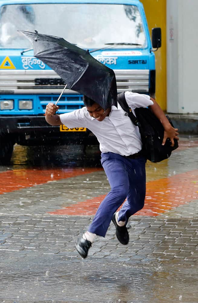 A school boy jumps over a puddle of water as it rains in Mumbai.