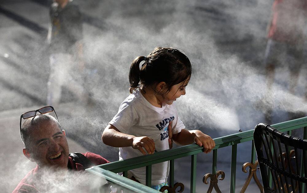 Tony Mener, left, holds his daughter Amelie Mener, 4, up to a mister to cool off along Las Vegas Boulevard, in Las Vegas. 