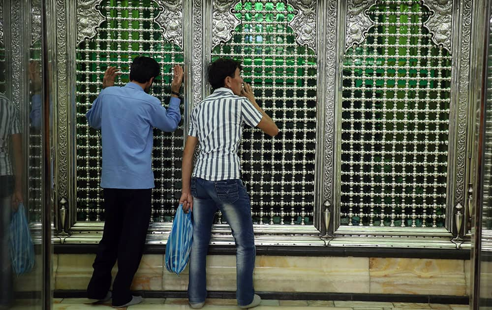 Two Shiite men pray as they touch bars of thegrave of the Shiite Saint Abdulazim during Muslim holy fasting month of Ramadan in Shahr-e-Ray, south of Tehran, Iran.