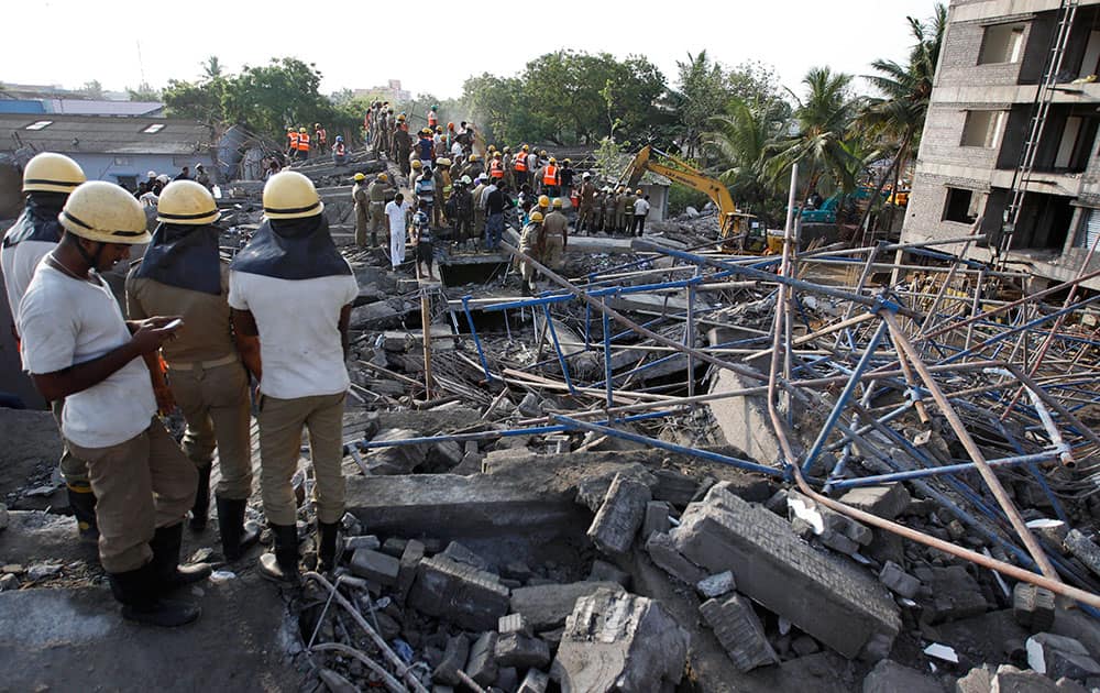 A rescuer, left checks his mobile phone as they search amid the rubble of a building that collapsed late Saturday during monsoon rains on the outskirts of Chennai, India. Police said dozens of workers have been pulled out so far and the search is continuing.