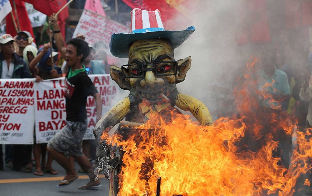 A Filipino activist runs beside a burning effigy of Philippine President Benigno Aquino III as they try to get near his house a day before the Comprehensive Agrarian Reform program expires in suburban Quezon city, north of Manila, Philippines.