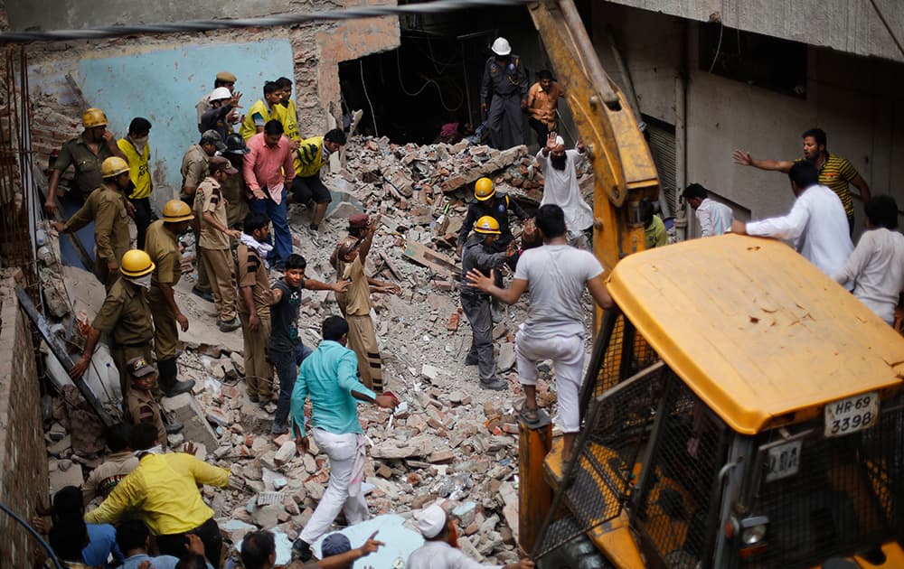 Rescuers gesture for an excavator to stop as they try to retrieve the body of a victim at the site of a building collapse in New Delhi.