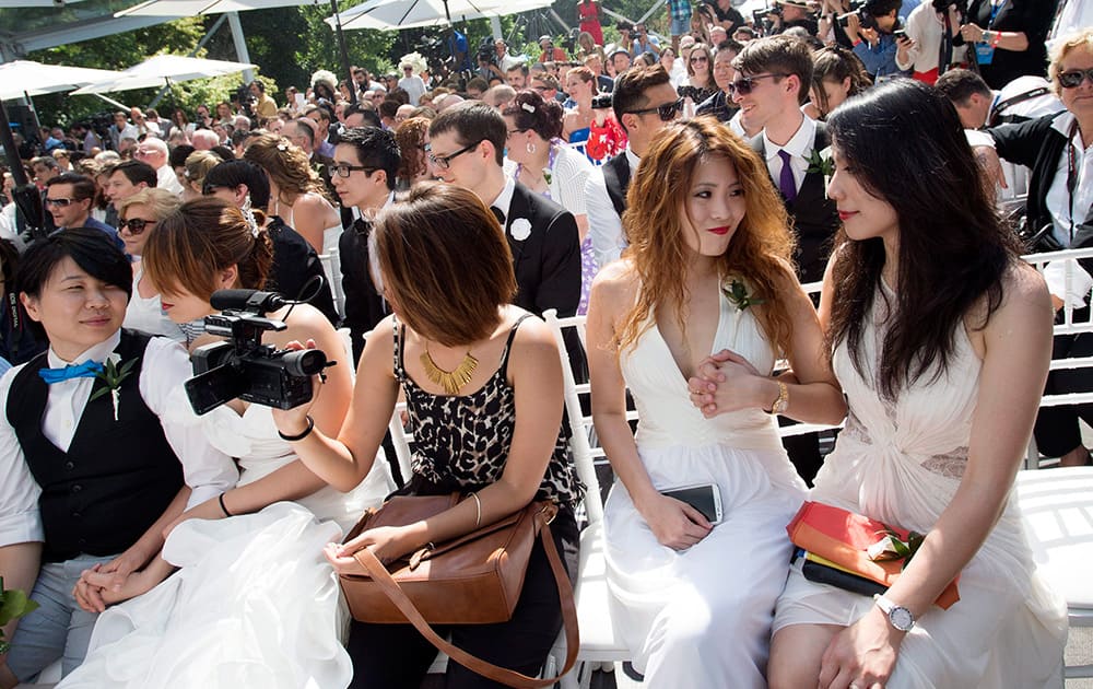 Cindy Su, second from left, holds the hand of her wife Lana Yu who flew from Taiwan to join over 100 gay couples in a mass wedding during World Pride 2014 at Casa Loma in Toronto.