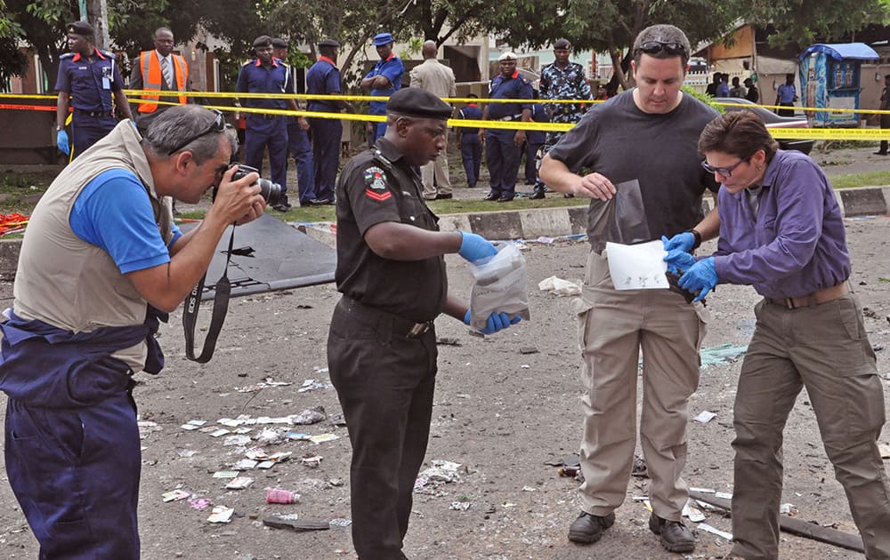 Unidentified security personnel assist a Nigerian troop to collect evidence at a explosion seen in Abuja, Nigeria. The National Hospital spokesman says a victim wounded in the bomb blast at a mall in Nigeria`s capital died overnight, raising the death toll to at least 22. 