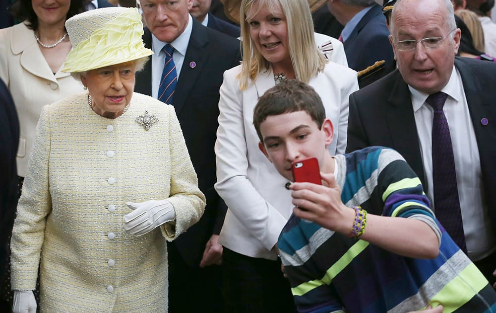 A local youth takes a selfie photograph in front of Queen Elizabeth II during a visit to St George`s indoor market on in Belfast.