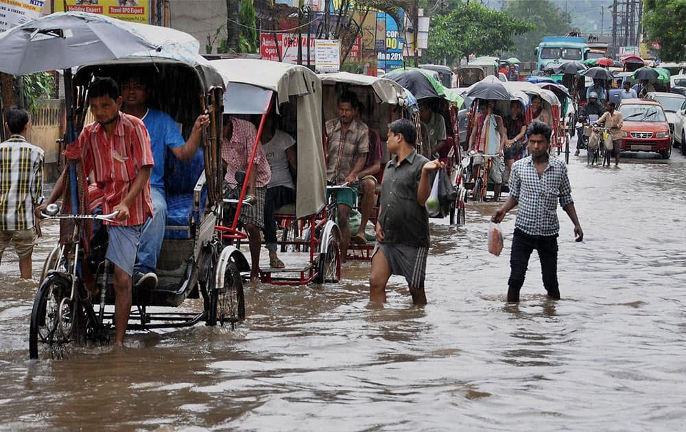 Rickshaw pullers and people walk through water logged road after a heavy rainfall in Guwahati.