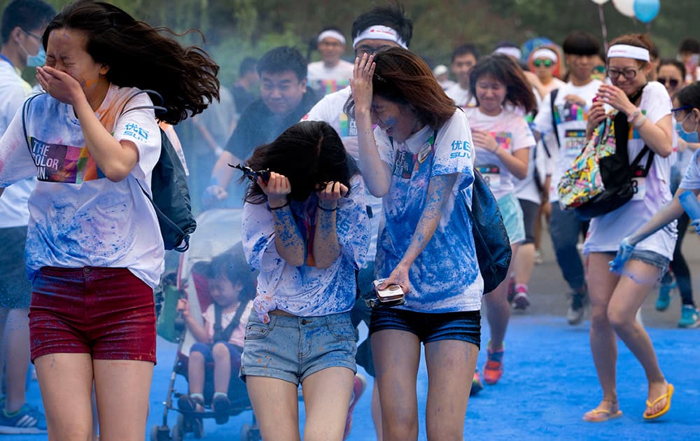 Participants try to cover themselves from color powder sprayed by volunteers as they run through a `color station` during a five-kilometer color run event held in Beijing, China.