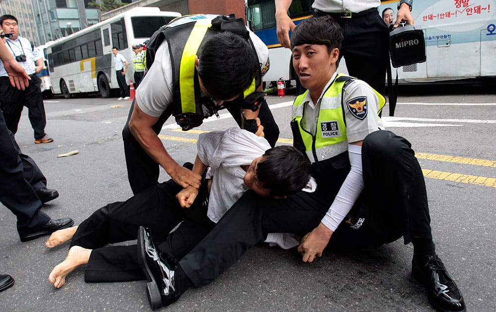 Police officers detain a protester as he tries to enter into Japanese Embassy during a rally against Japan`s plan to reform its constitution in Seoul, South Korea.