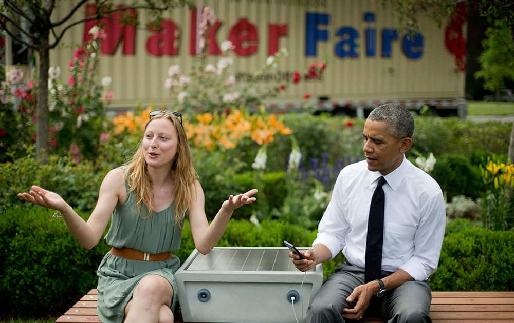 President Barack Obama holds up cell phone that is plugged into a `soofa` a solar powered bench, that Sandra Richter of Cambridge, Mass., helped designed with allows people to charge their phones, during his meeting with students, entrepreneurs and inventors on the South Lawn of the White House in Washington.