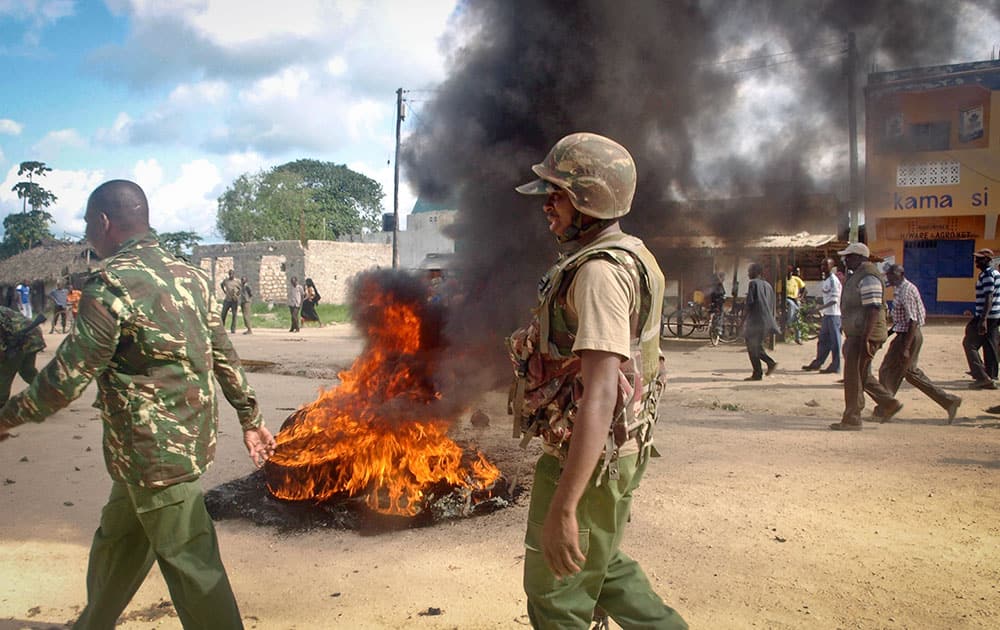 Armed security forces walk past a barricade of burning tyres set up by residents to protest against the recent killings and what they claimed was the government`s failure to provide them with enough security, in the village of Kibaoni just outside the town of Mpeketoni, about 60 miles (100 kilometers) from the Somali border on the coast of Kenya.