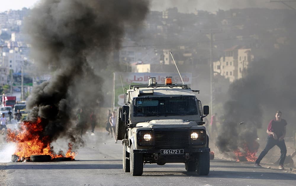 An Israeli army vehicle drives past burning tires during a search operation in the West Bank refugee camp of Jenin. Israeli security forces searched the West Bank looking for three missing Israeli teenagers who they fear have been abducted by Palestinian militants.