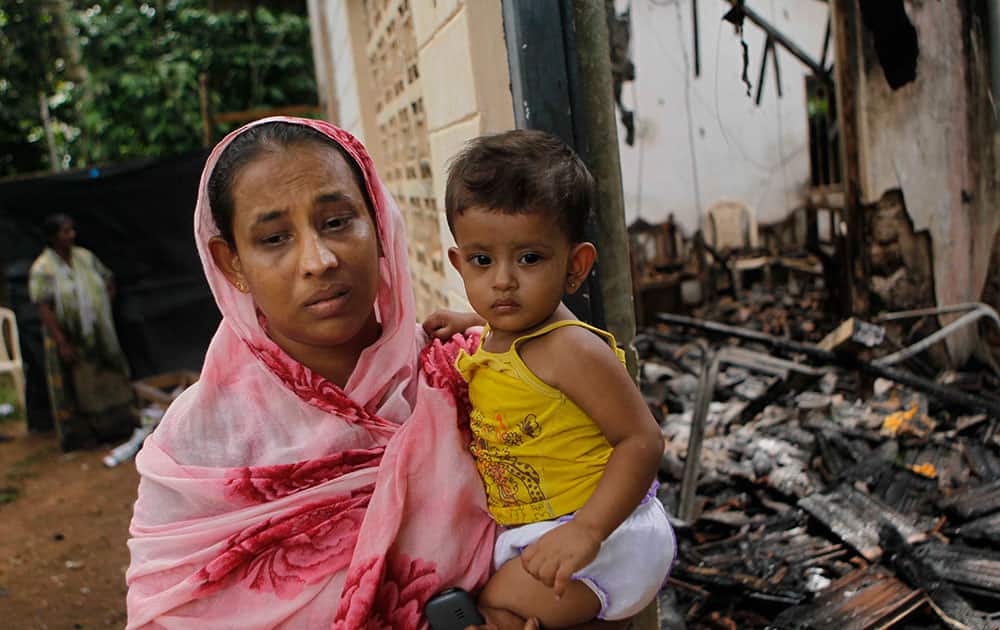 A Sri Lankan Muslim woman carries her daughter while standing outside her burnt house in Adhikarigoda , a village near Aluthgama town, 50 kilometers (31.25 miles) south of Colombo, Sri Lanka. At least three Muslims were killed after a right-wing Buddhist group with alleged state backing clashed with Muslims in southwestern Sri Lanka, a government minister said Monday. Dozens of shops were burned, homes looted and some mosques attacked in the violence Sunday night in the town of Aluthgama, local residents said.