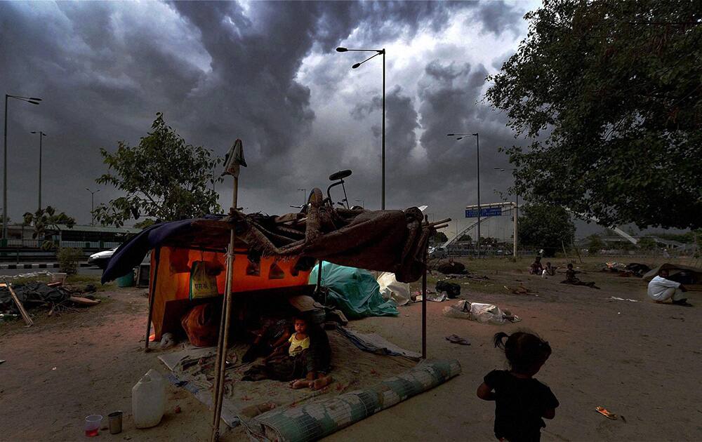 Children of laborers at a road side as dark clouds hovering in New Delhi.