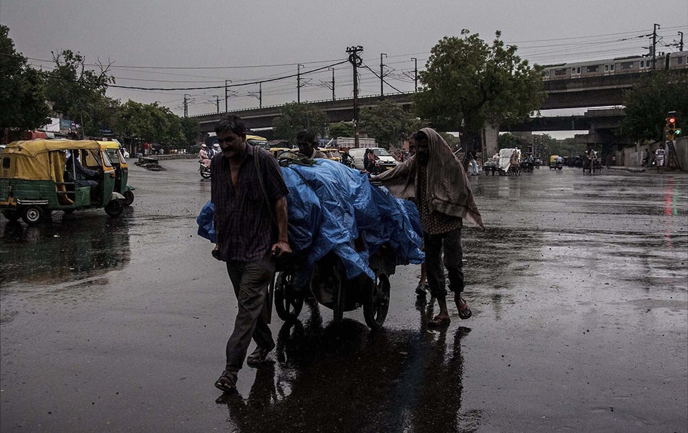 Labourers move a cart along a road amid rains in New Delhi.