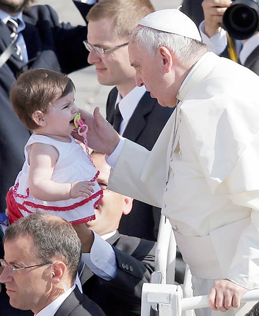 Pope Francis caresses a child as he is driven through the crowd during his weekly general audience in St. Peter`s Square at the Vatican.