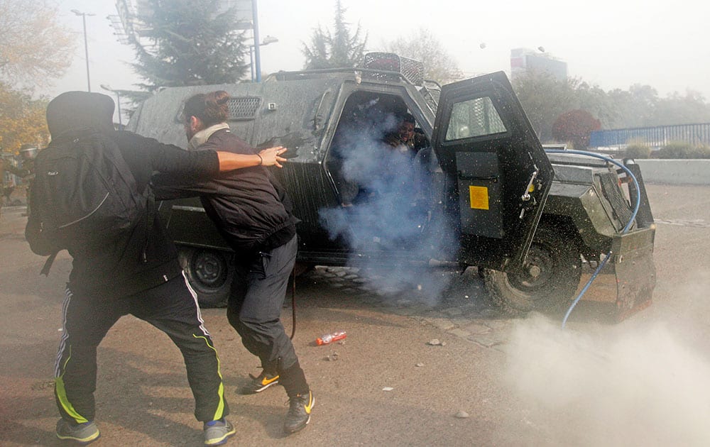 A police officer, is attacked by protesters after he opened the door of his armored car to throw a tear gas grenade in the courtyard of the University of Santiago, in Santiago, Chile.