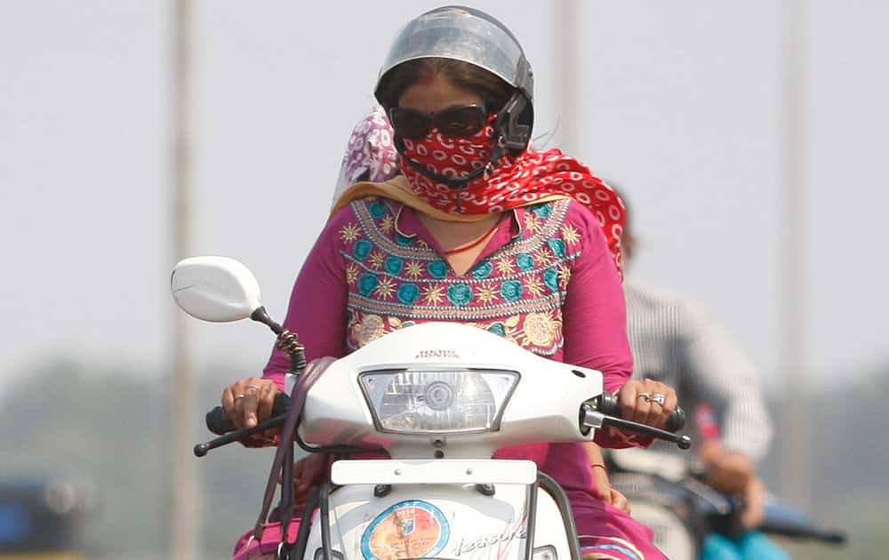 A woman shields her face with a piece of cloth to protect from the heat, as she rides a two wheeler on a hot summer day in Jammu.