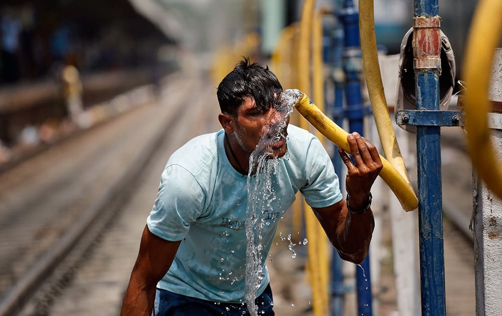 A commuter splashes water from a pipe onto his face to get respite from the heat at the railway station in Allahabad.