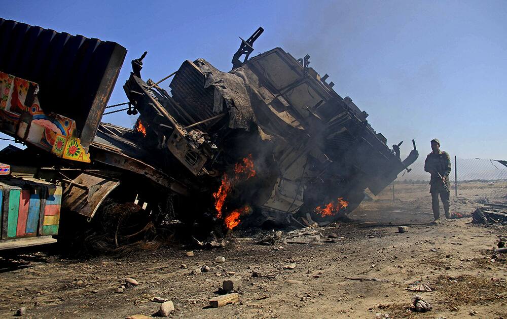 An Afghan policeman stands near a burning NATO supply truck in Behsud district of Jalalabad east of Kabul, Afghanistan. An Afghan provincial official says suicide bombers have attacked a parking lot at a police base in eastern Afghanistan, killing a guard and setting almost two dozen trucks ablaze.