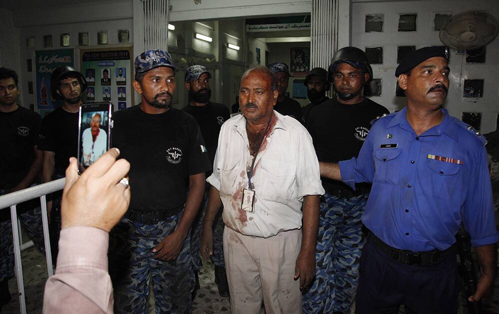 Pakistani airport security staff help an injured airlines employee, center, to leave a terminal following attacks by gunmen the Jinnah International Airport in Karachi, Pakistan.