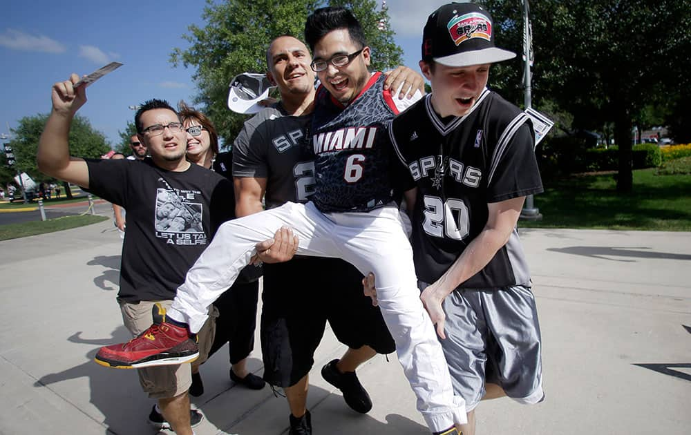 San Antonio Spurs fabs Michael Common, second from left, and Sam Gutierrez, right, carry Mark Lopez who wears Miami Heat forward LeBron James` jersey as they arrive for Game 2 of the NBA basketball finals in San Antonio.